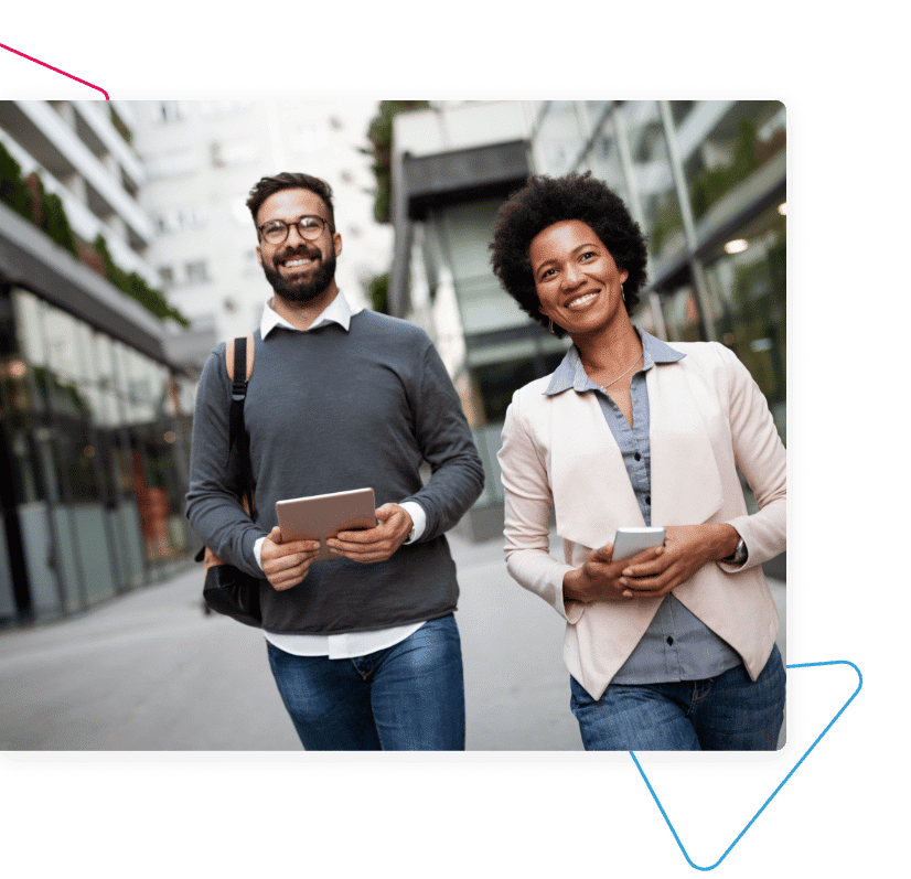 woman holding mobile and man holding tablet walking down a street