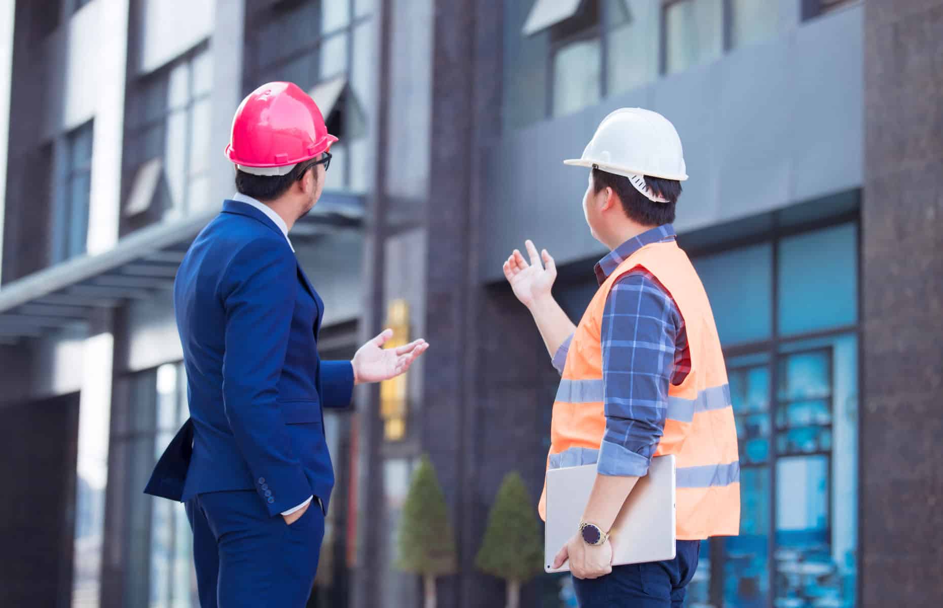 Two men wearing hard hats looking at a building.
