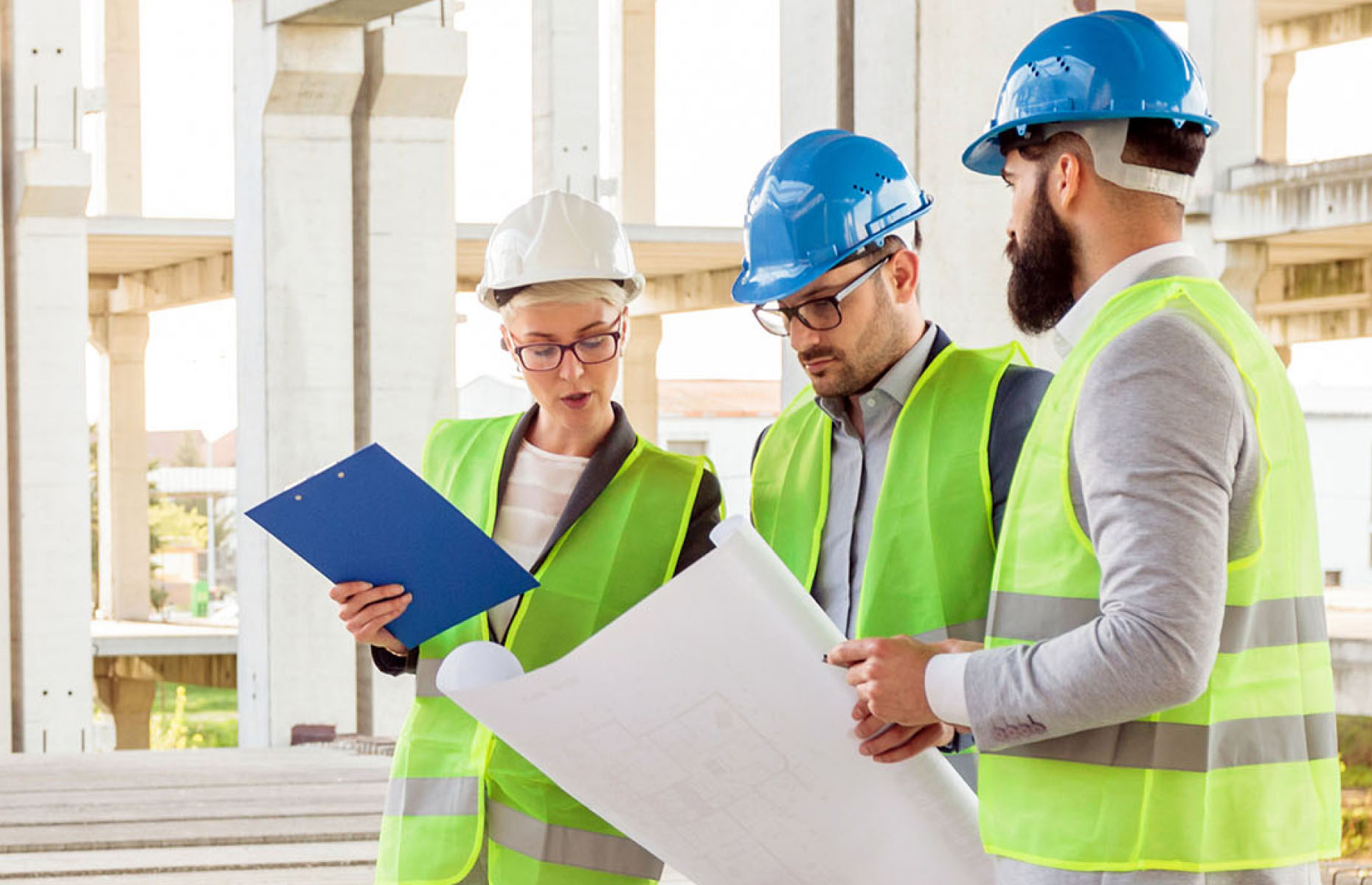 Three people in hard hats looking at plans inside a construction site.